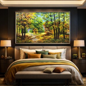May include: A large framed landscape painting of a forest scene with a path. The painting hangs above a bed with a gray headboard, white pillows, and a mustard-colored blanket. Two lamps sit on nightstands.