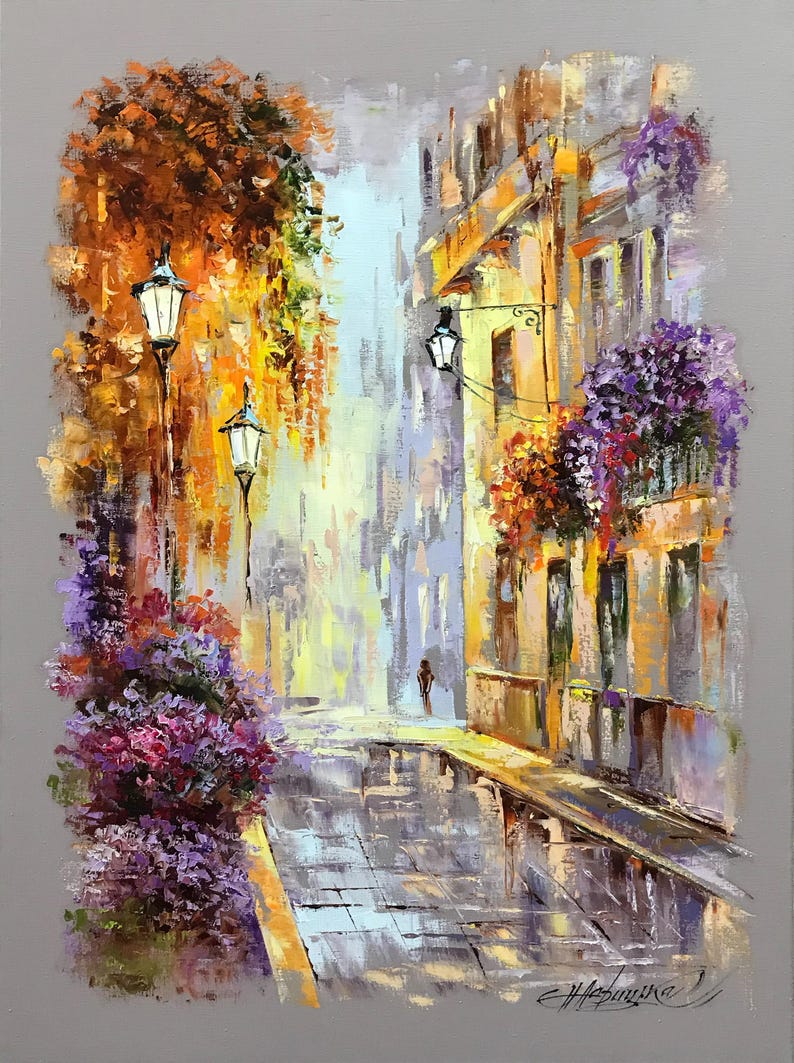 May include: Oil painting of a European street scene with a cobblestone road. The buildings are yellow and orange with purple flowers. Street lamps and trees are also visible. A person is walking down the street.