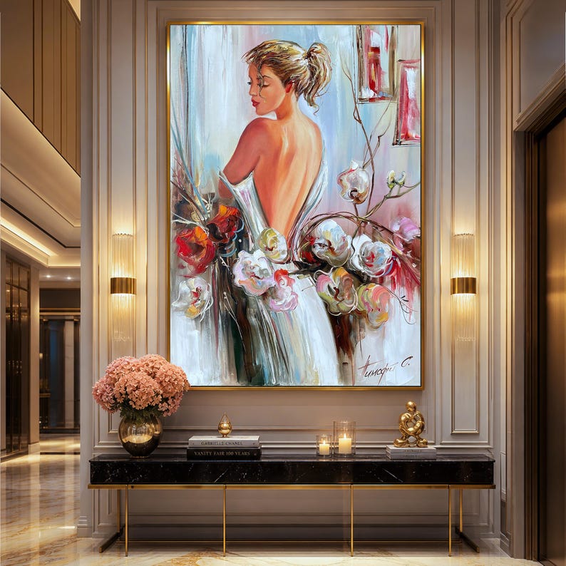 May include: An oil painting of a woman in a white dress with a low back, standing near flowers. The artwork features a gold frame and is displayed in a well-lit hallway. The color palette includes white, red, and pink.