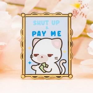 May include: Gold-coloured enamel pin featuring a white cat holding money with the text "Shut Up & Pay Me" in a blue and white frame.