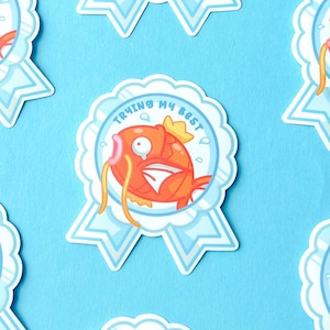 Könnte beinhalten: Sieben blaue und weiße Bandaufkleber mit einem orangefarbenen Cartoon-Fisch mit einer Krone auf dem Kopf. Der Text auf den Aufklebern lautet "Trying My Best".