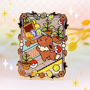 May include: A rectangular enamel pin featuring a brown Eevee character in a garden scene. The pin has a decorative border with flowers and leaves. The scene includes potted plants, coins, and a Poké Ball.