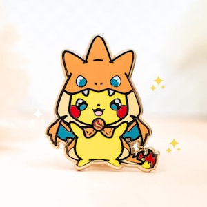 May include: A yellow enamel pin featuring a Pikachu character dressed in a Charizard costume. The pin has a gold outline, orange and blue accents, and a small flame detail. The design includes a bow tie and sparkling star details.