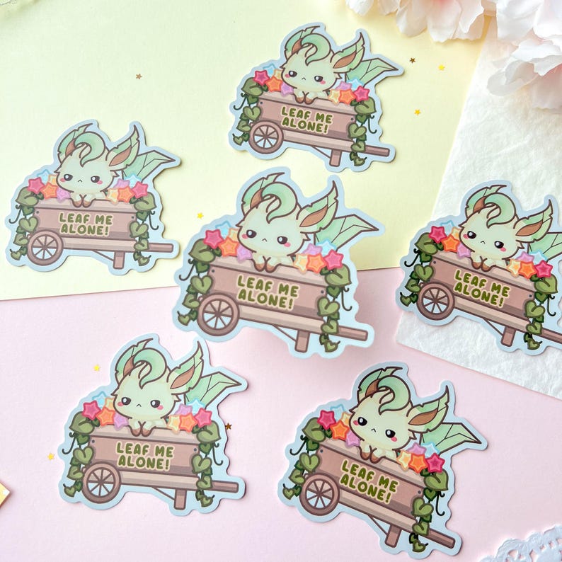 May include: A collection of stickers featuring a cartoon creature with green and cream coloring, with large ears and wings, in a wooden wheelbarrow filled with colorful stars and flowers. The wheelbarrow has the text "LEAF ME ALONE!"