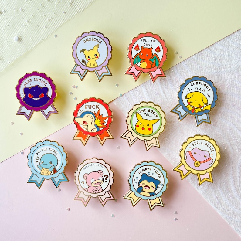 May include: Nine enamel pins featuring Pokemon characters with humorous phrases. The pins are in the shape of a gold ribbon with a circular center. The phrases on the pins are "Dead Inside", "Anxious", "Full of Rage", "Corporate Slave", "Fuck", "One Brain Cell", "Still Alive", "Did the Thing", "Procrastinator", and "Always Tired".
