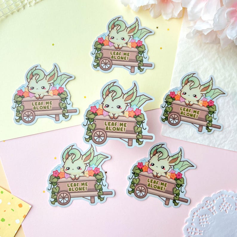 May include: A collection of stickers featuring a cartoon creature with green and cream coloring, large ears, and a small cart filled with flowers. The cart has the text "LEAF ME ALONE!" on it.