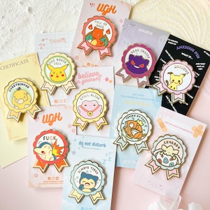 May include: A collection of 10 enamel pins featuring various cartoon characters and humorous phrases. The pins are gold-colored and have a ribbon design. Some of the phrases include "Full of Rage", "Dead Inside", "Trying My Best", "Overthinker", "One Brain Cell", "Still Alive", "Do Not Disturb", "Always Tired", "Anxious Pin", "Crybaby", and "Fuck".
