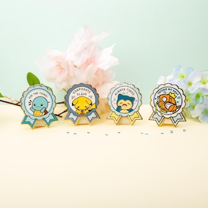 May include: Four enamel pins featuring cartoon characters from the Pokemon franchise. Each pin is shaped like a blue and yellow ribbon with a different slogan. The slogans are "Did the thing!", "Corporate Slave", "Always Tired", and "Toking My Best".