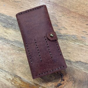May include: A brown leather wallet with a flap closure and a brass button. The wallet has multiple stitched compartments and a textured surface.