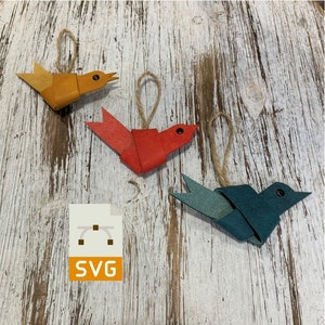 May include: Three handmade leather bird ornaments in orange, red, and blue. The ornaments are hanging from twine and have a rustic, handmade look.