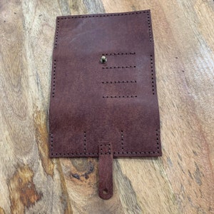 May include: A brown leather wallet with a flap closure and a small strap. The wallet has multiple card slots and a pocket for cash.