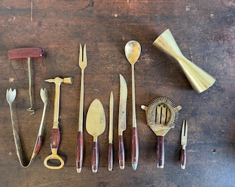 Op de afbeelding: Een set messing baraccessoires bestaande uit een kurkentrekker met donkerhouten handvat, ijstang, flesopener-hamer, vork met lange steel, kleine schep, mes, lepel met lange steel, cocktailzeef en een jigger.