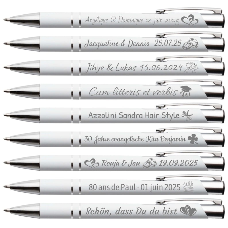 Op de afbeelding: Een verzameling witte pennen met zilveren details. Elke pen is gegraveerd met gepersonaliseerde tekst en decoratieve iconen. De pennen tonen namen, data en zinnen, waaronder "Ang&eacute;lique & Dominique", "Jacqueline & Dennis" en "Sch&ouml;n, dass Du da bist".