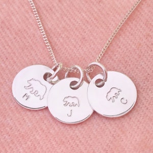 May include: Silver necklace with three round charms featuring bear silhouettes and the letters M, J, and C.