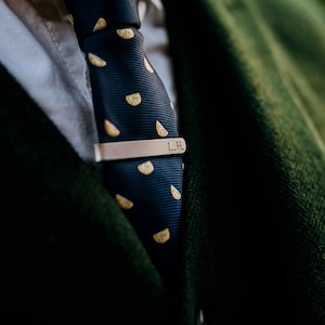 May include: A navy blue tie with a lemon pattern and a gold tie clip engraved with the initials "L.H."
