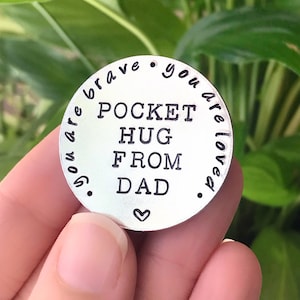 Op de afbeelding: Zilveren zaktoken met de tekst "You are brave. You are loved. Pocket hug from Dad."