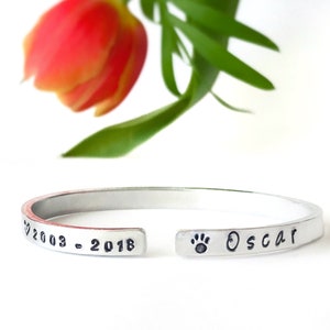 May include: Silver cuff bracelet engraved with the inscription "2003 - 2018" and a paw print with the name "Oscar".
