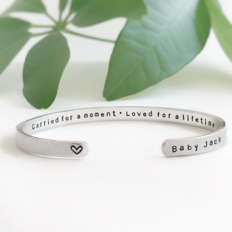 May include: Silver bangle bracelet with the inscription "Carried for a moment. Loved for a lifetime" and a small heart charm. The bracelet also has the inscription "Baby Jack" on the other side.