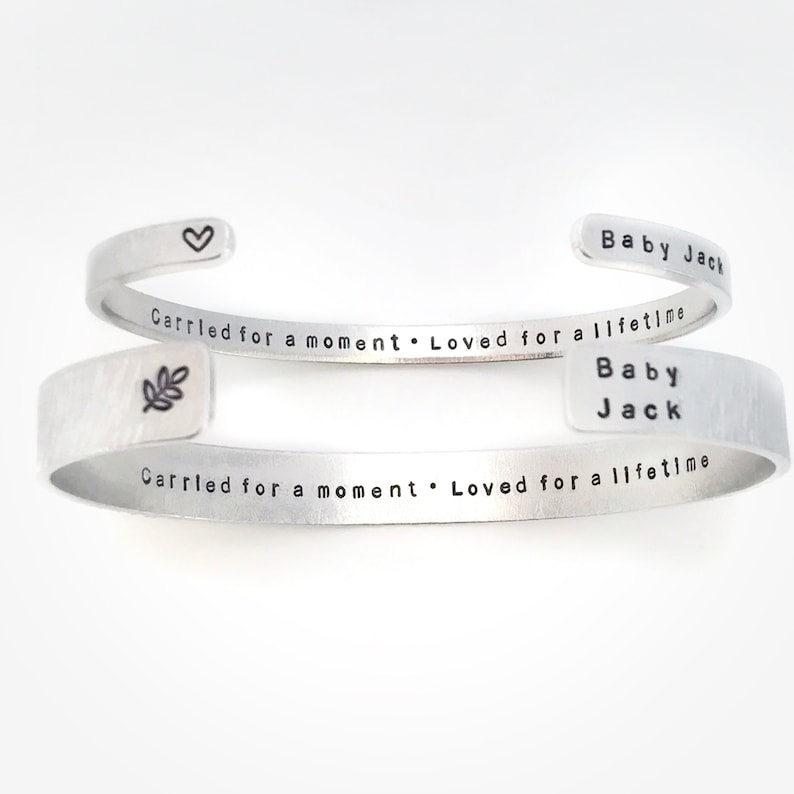 May include: Two silver bracelets with the inscription "Carried for a moment. Loved for a lifetime" and the name "Baby Jack" engraved on each. The bracelets are stacked on top of each other.