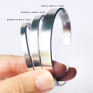 May include: Three silver metal bracelets of different widths. The bracelets are stacked on top of each other. The largest bracelet is 9 mm wide and 17.5 cm long. The middle bracelet is 6 mm wide and 15 cm long. The smallest bracelet is 4 mm wide and 15 cm long.