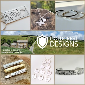 May include: A collection of handcrafted jewelry and accessories. Includes a silver keychain with a mountain and camping scene, a bee pendant necklace, two silver bracelets, and a tie clip with the date "10.08.25". The image also features a necklace with multiple small pendants.