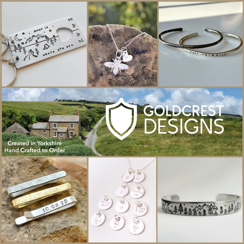 May include: A collection of handcrafted jewelry and accessories. Includes a silver keychain with a mountain and camping scene, a bee pendant necklace, two silver bracelets, and a tie clip with the date "10.08.25". The image also features a necklace with multiple small pendants.