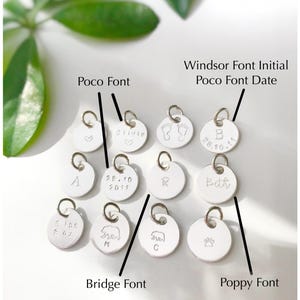 May include: A collection of silver charms with different fonts and designs. The charms include a heart, a footprint, a bear, a paw print, and the letters A, B, R, and the names Olivia and Beth. The date 28.10.11 is also included on one of the charms. The charms are labeled with the fonts Poco, Windsor, Bridge, and Poppy.