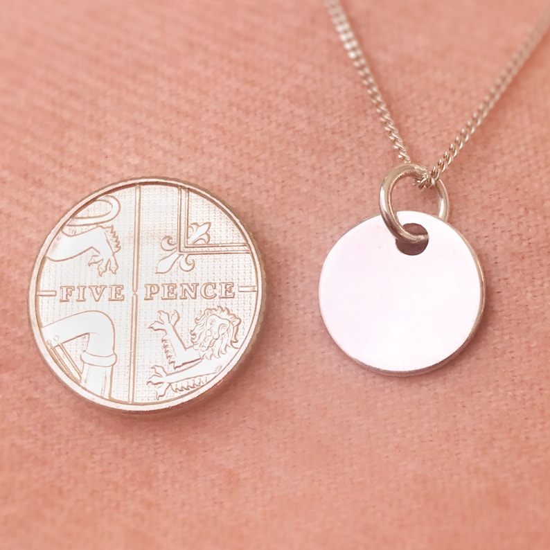 May include: A silver necklace with a round pendant featuring the inscription "FIVE PENCE". The pendant is attached to a silver chain.