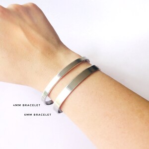 May include: Two silver bracelets on a person's wrist. The top bracelet is labeled "4MM BRACELET" and the bottom bracelet is labeled "6MM BRACELET".