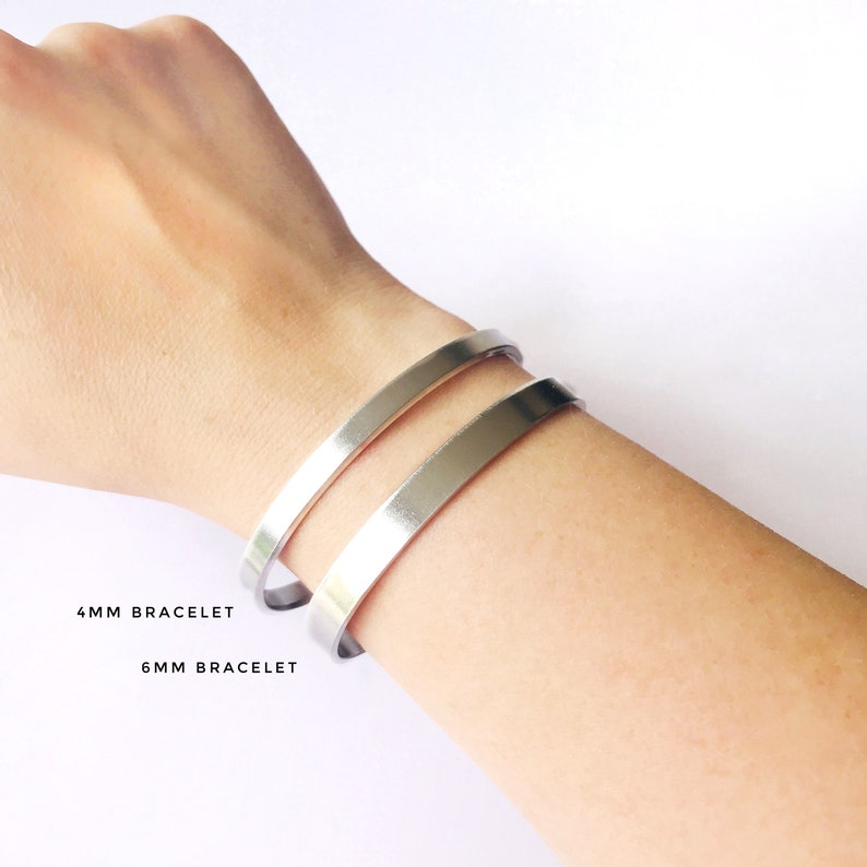 May include: Two silver bracelets on a person's wrist. The top bracelet is labeled "4MM BRACELET" and the bottom bracelet is labeled "6MM BRACELET".