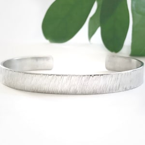May include: A silver textured bangle bracelet. The bracelet is made of metal and has a hammered finish.