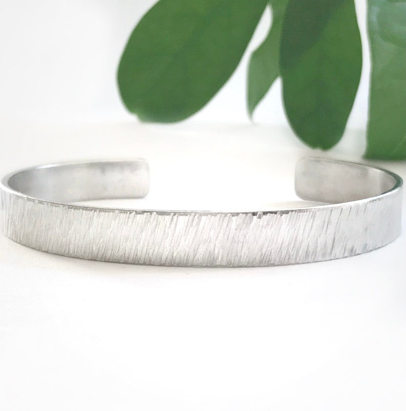 May include: A silver textured bangle bracelet. The bracelet is made of metal and has a hammered finish.