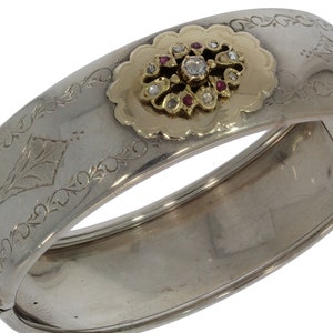 May include: A silver bangle bracelet featuring an ornate gold and diamond design. The bracelet is engraved with floral patterns.