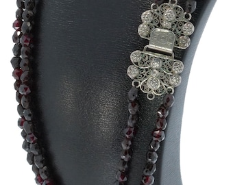 May include: A triple strand necklace made of dark red garnet beads with a silver filigree clasp.