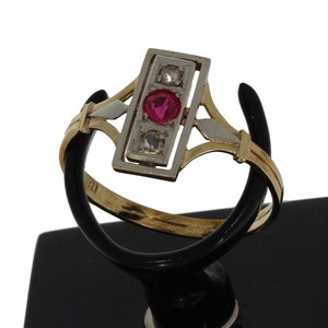 May include: A gold and silver ring with a red gemstone and two smaller white gemstones set in a rectangular frame.