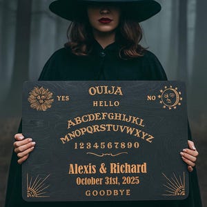 Op de afbeelding: Een zwart Ouija-bord met gouden letters en afbeeldingen wordt vastgehouden door een persoon die een zwarte heksenhoed en cape draagt. Het bord bevat het alfabet, cijfers en de namen Alexis & Richard, met de datum 31 oktober 2025.