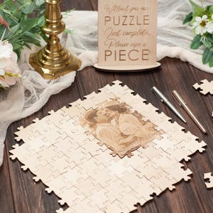 Peut inclure: Un puzzle en bois avec une photo de couple. Le puzzle est sur une table en bois avec deux stylos et une pancarte qui dit "Sans toi, notre puzzle n'est pas complet. Veuillez signer un morceau."
