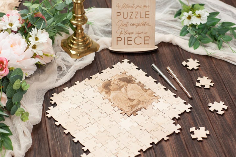 Peut inclure: Un puzzle en bois avec une photo de couple. Le puzzle est sur une table en bois avec deux stylos et une pancarte qui dit "Sans toi, notre puzzle n'est pas complet. Veuillez signer un morceau."