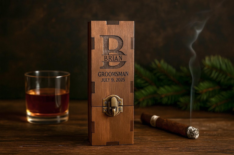 May include: A wooden box with the name "Brian", the word "Groomsman", and the date "July 9, 2025" engraved on it. A glass of amber liquid, a lit cigar, and smoke are also visible. The box has a metal clasp.