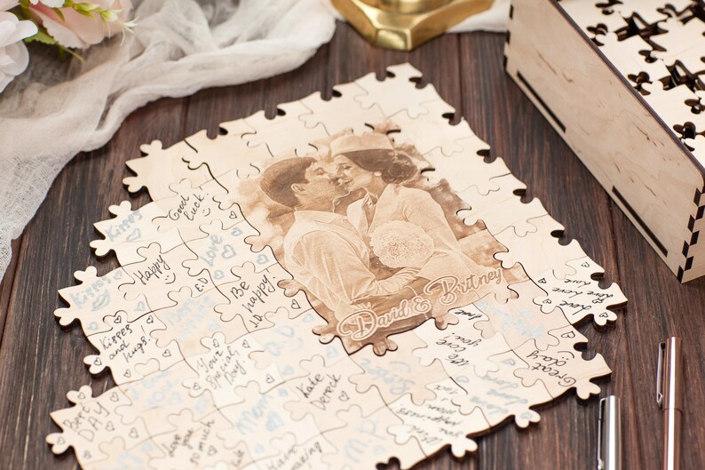 Peut inclure: Un puzzle en bois avec une photo d'un couple imprim&eacute;e dessus. Le puzzle est assembl&eacute; et a un fond blanc avec des c&oelig;urs bleus et des messages &eacute;crits &agrave; la main. Les noms du couple sont &eacute;crits sur le puzzle, "David & Britney".