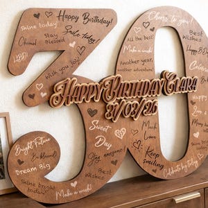 Könnte beinhalten: Eine hölzerne Geburtstagsdekoration in Form der Zahl 30. Die Zahlen sind braun mit eingraviertem Text und Herzen. Die Worte "Happy Birthday Clara" und das Datum stehen im Zentrum.