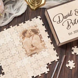 Peut inclure: Une bo&icirc;te &agrave; puzzle en bois avec une inscription personnalis&eacute;e "David & Britney Est. 2022" et une photo de couple. La bo&icirc;te &agrave; puzzle est sur une surface en bois avec une pi&egrave;ce de puzzle blanche et un stylo.
