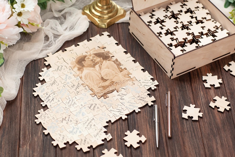 Peut inclure: Un puzzle en bois avec une photo de couple imprim&eacute;e dessus. Le puzzle est assembl&eacute; et a une bo&icirc;te en bois &agrave; c&ocirc;t&eacute;. Les pi&egrave;ces du puzzle sont dispers&eacute;es autour de la bo&icirc;te. Deux stylos sont &eacute;galement sur la table.