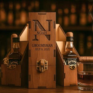 May include: A wooden gift box with the name "NOAH" and the text "Groomsman July 9, 2025" engraved on the front. The box holds two miniature whiskey bottles and a glass of whiskey with a cigar resting on the rim.