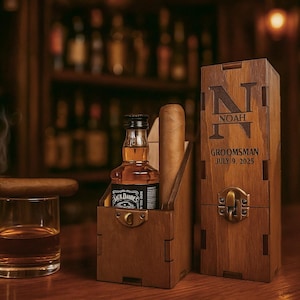 May include: A wooden groomsman gift set featuring a miniature bottle of Jack Daniel's, a cigar, and a rocks glass with amber liquid. The set includes a personalized wooden box with the name "NOAH" and the date "JULY 9, 2025".