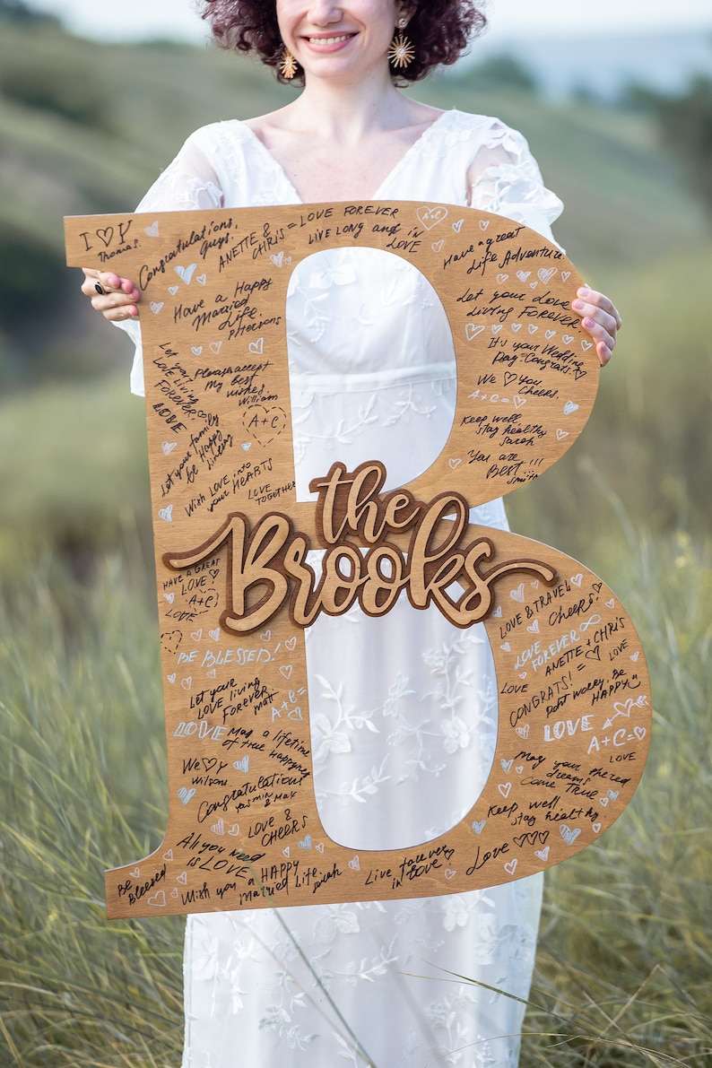 Pu&ograve; includere: Un cartello di legno a forma della lettera B con le parole "the Brooks" scritte in corsivo. Il cartello &egrave; decorato con cuori e messaggi scritti con un pennarello nero.
