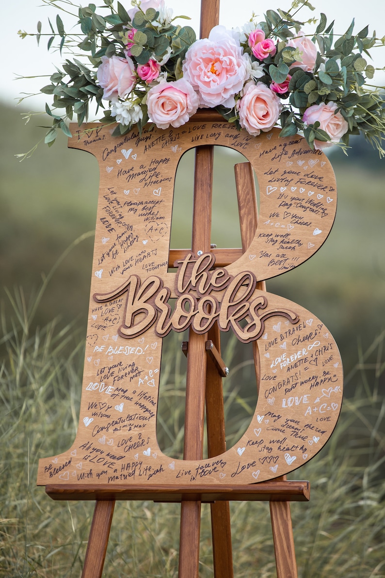 Pu&ograve; includere: Un cartello di legno a forma delle lettere "B" ed "R" con le parole "The Brooks" in mezzo. Il cartello &egrave; decorato con fiori e ha molti messaggi scritti a mano.