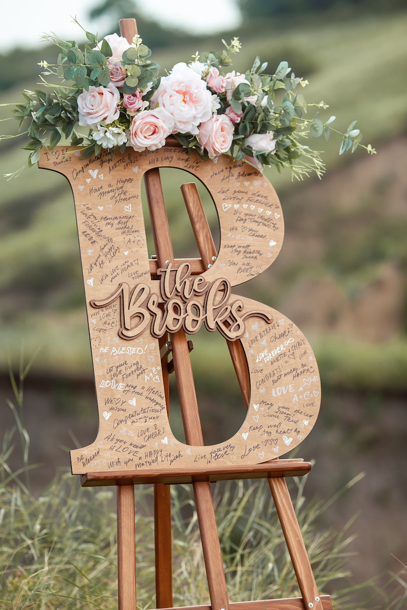 Pu&ograve; includere: Un cartello di legno a forma delle lettere "B" e "B" con il testo "the Brooks" al centro. Il cartello &egrave; decorato con fiori e ha molti messaggi scritti a mano.