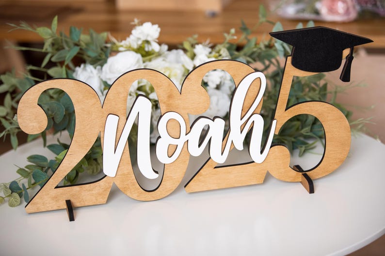 May include: Wooden 2023 graduation sign with the name Noah in white lettering and a black graduation cap on top.