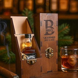 May include: A wooden gift box with a small bottle of Jack Daniel's whiskey inside. The box is open, revealing the bottle and a decorative interior. A cigar and a glass of whiskey are also present.